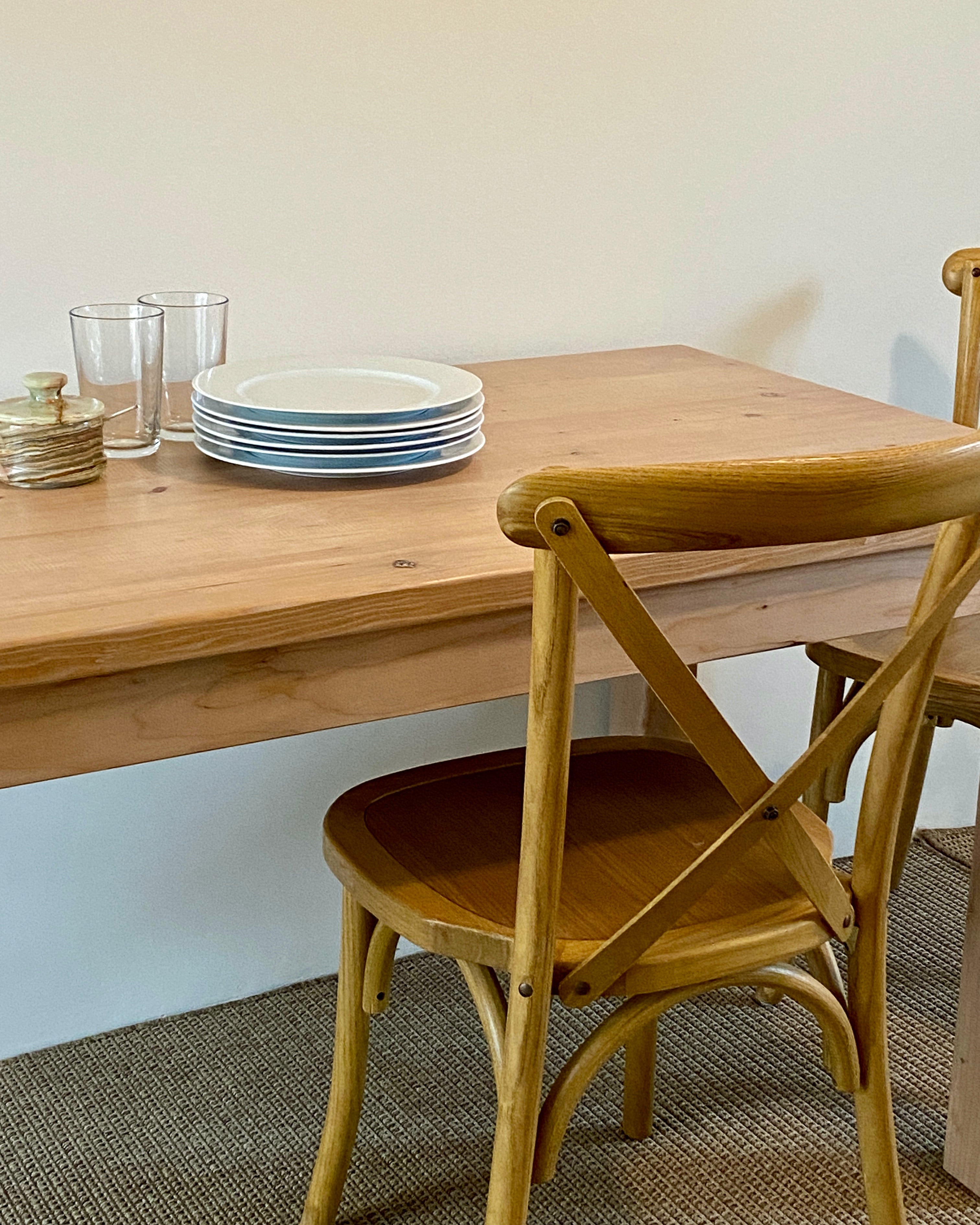 A rectangular reclaimed wood parsons dining table with a straight leg design, displayed in a home setting with plates and glasses on top.