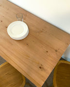 A rectangular reclaimed wood parsons dining table with a straight leg design, displayed in a home setting with plates and glasses on top. Table top view.