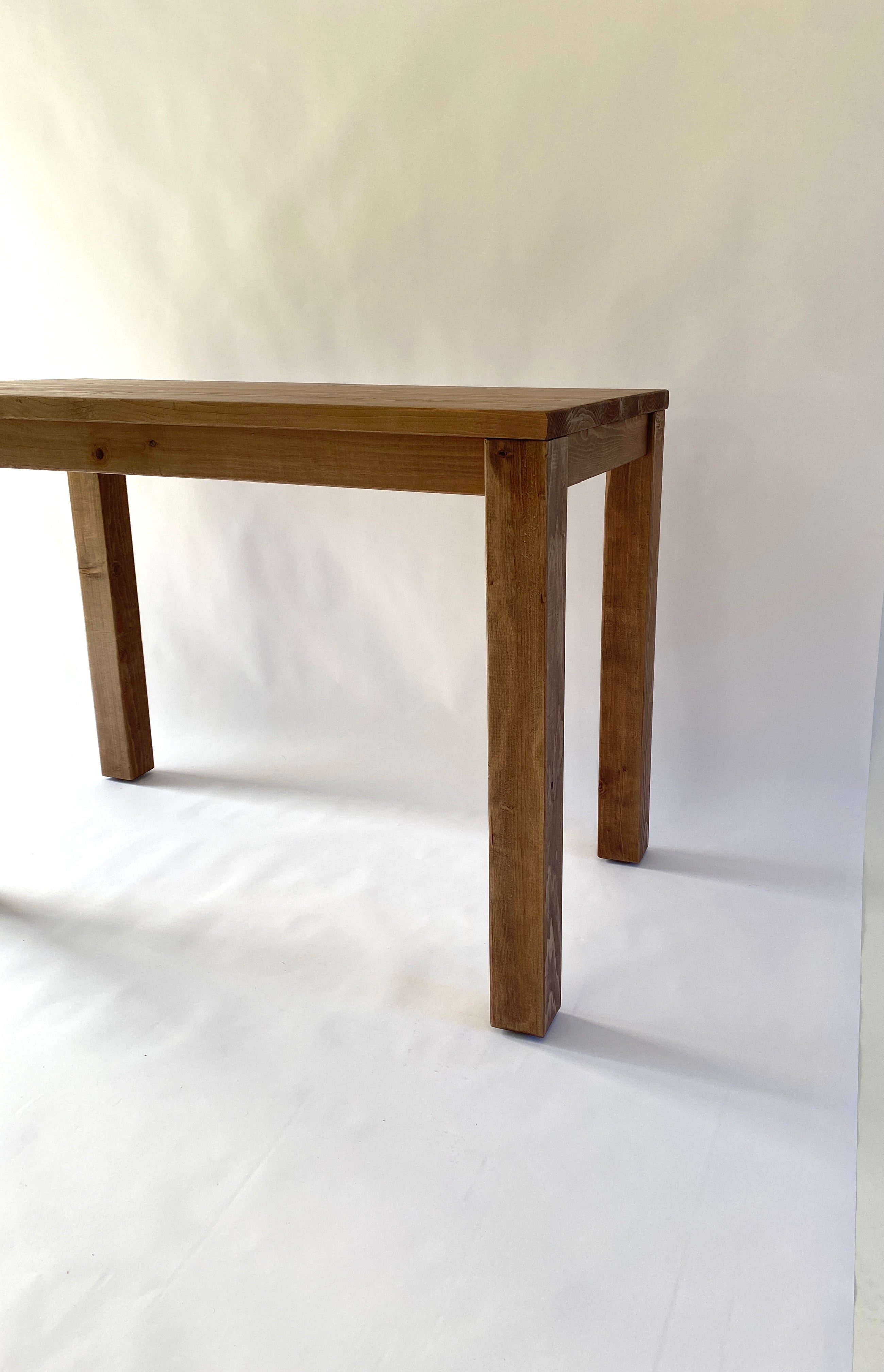 A Parsons kitchen island table made of solid wood with a straight leg design, displayed alongside a wooden stool. The table has a medium brown wood finish and is placed against a neutral background.
