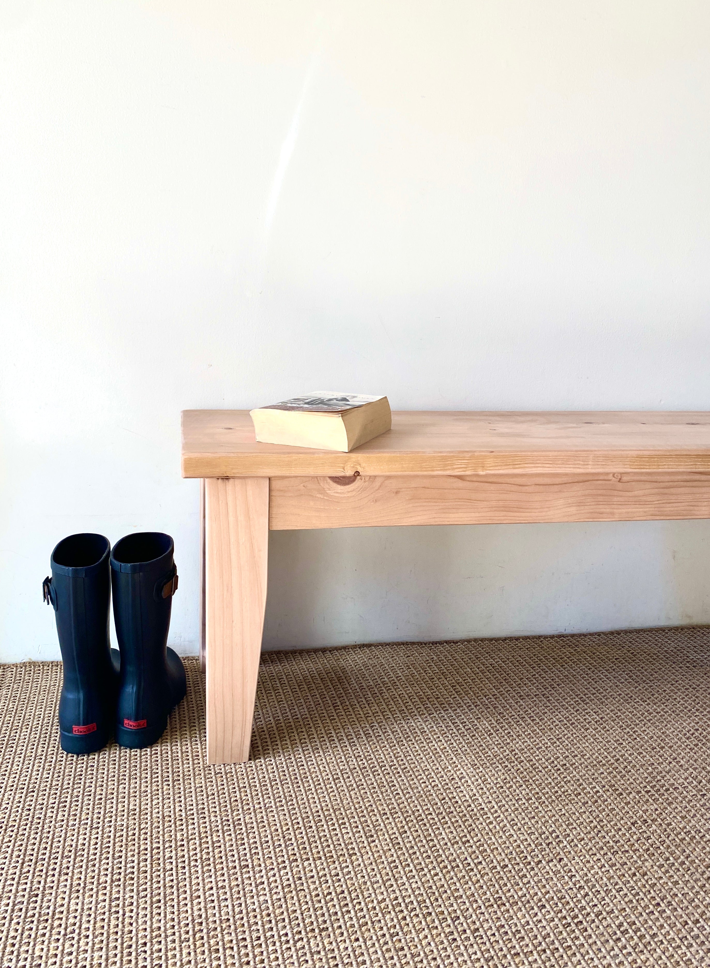 A Provincial Wood Bench made of reclaimed wood, displayed in a room setting with a pair of boots placed against it.
